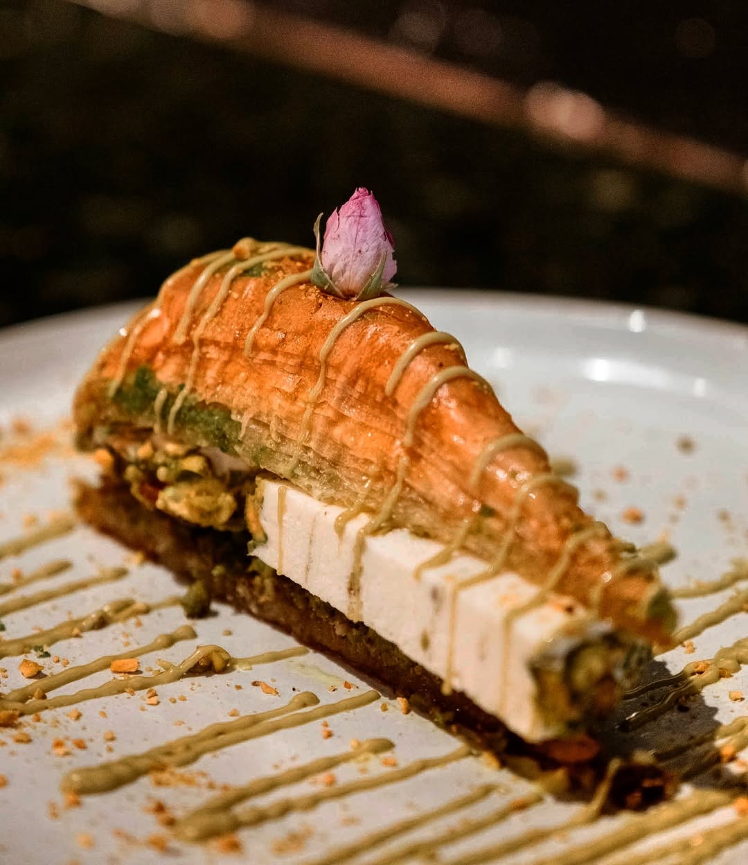 Layered Middle Eastern pastry with cream, pistachio drizzle and rose garnish