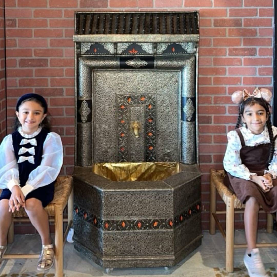 Sham and Yasmeen seated by a traditional Middle Eastern fountain